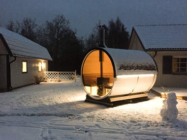 Sauna a botte in un ambiente innevato con illuminazione interna.