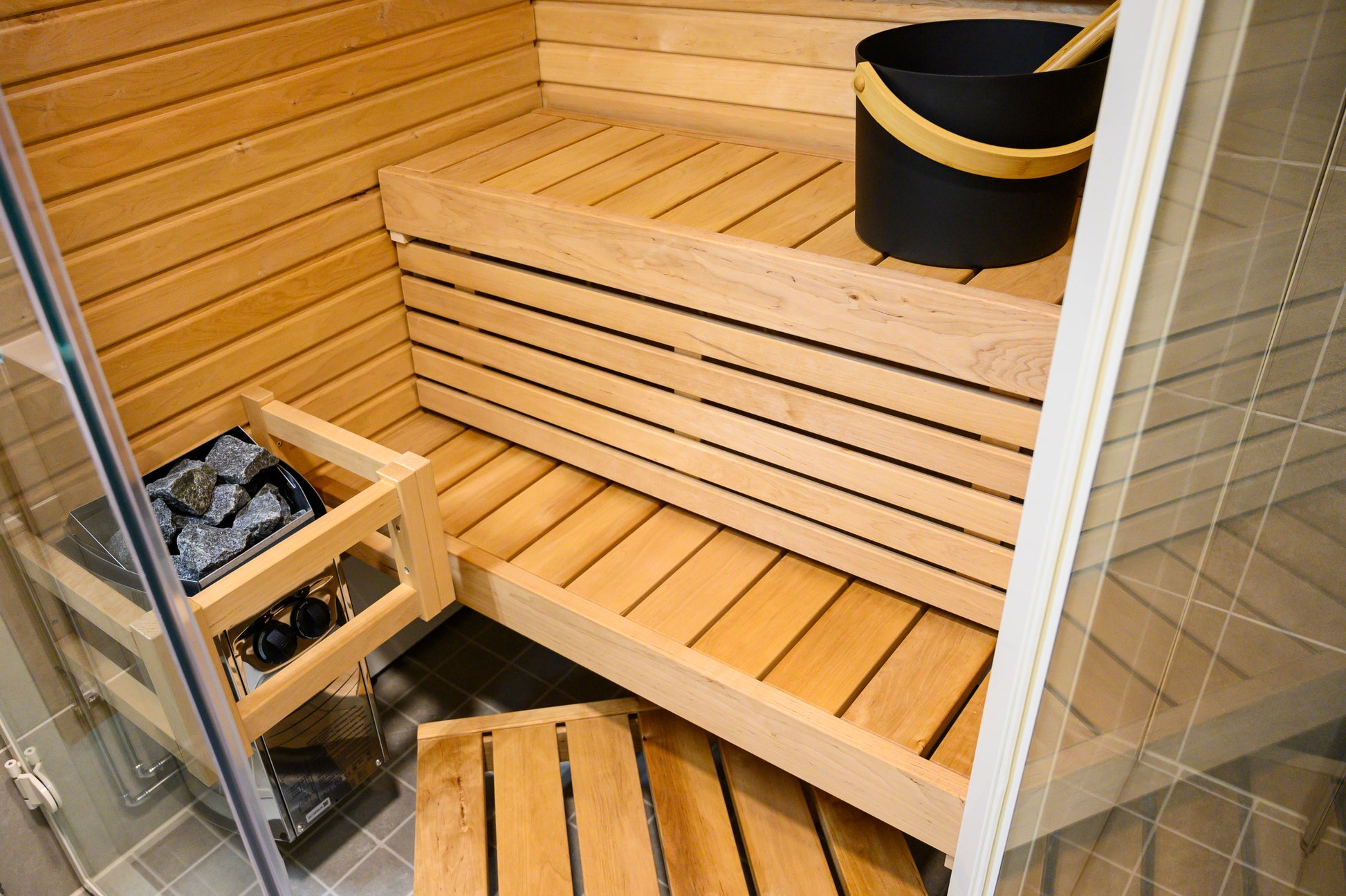 Sauna angolare Sirius con panche in legno e secchio nero.