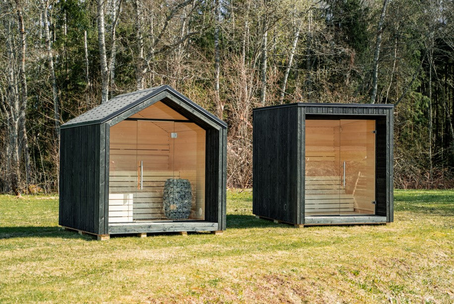 Sauna esterna LUMI isolata con una porta di vetro, in un'area verde.